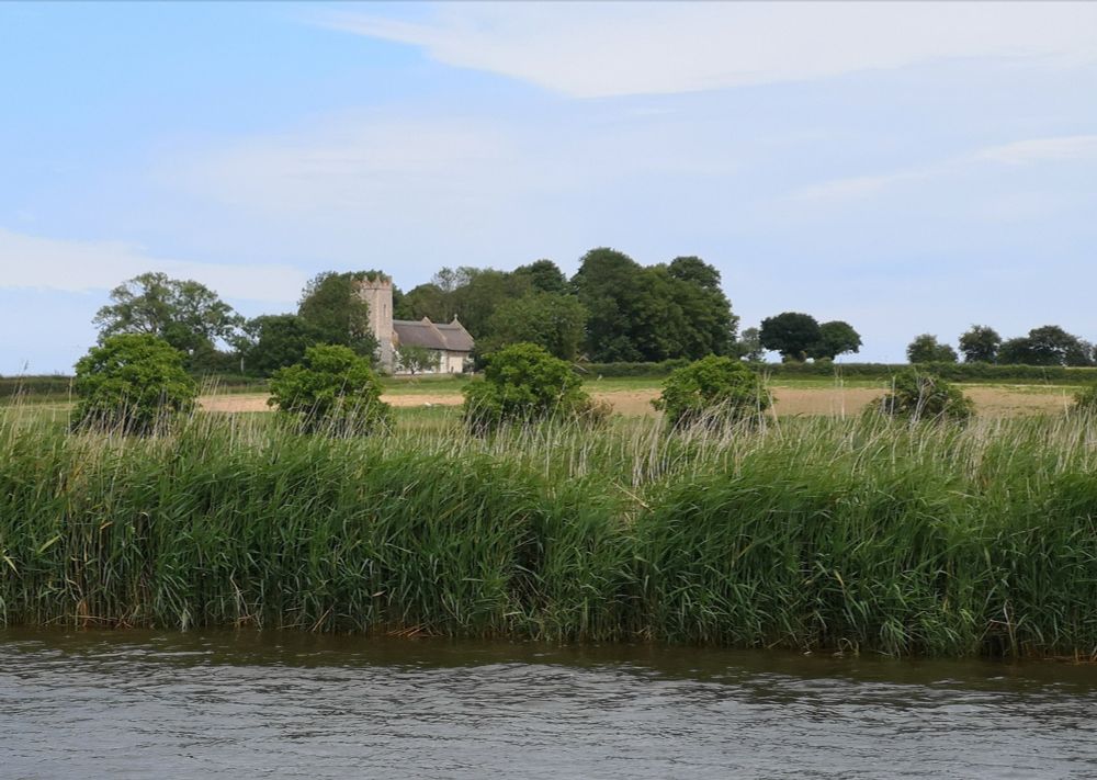 Thurne church sitting in fields and as seen from a boat of the River Thurne.