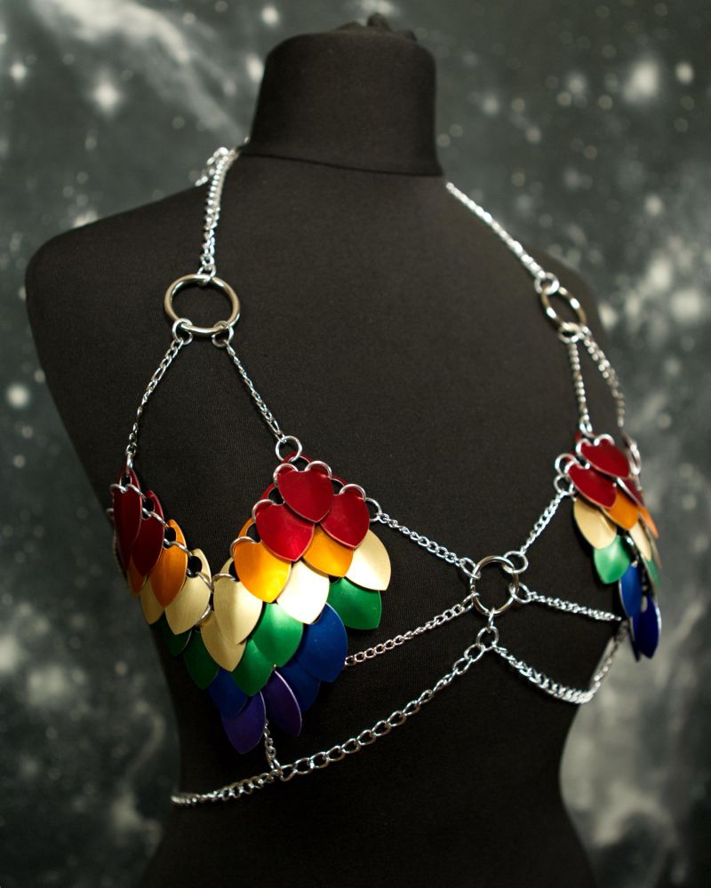 A rainbow scale mail heart shaped top on a black dressmaker doll, in front of a space themed backdrop 