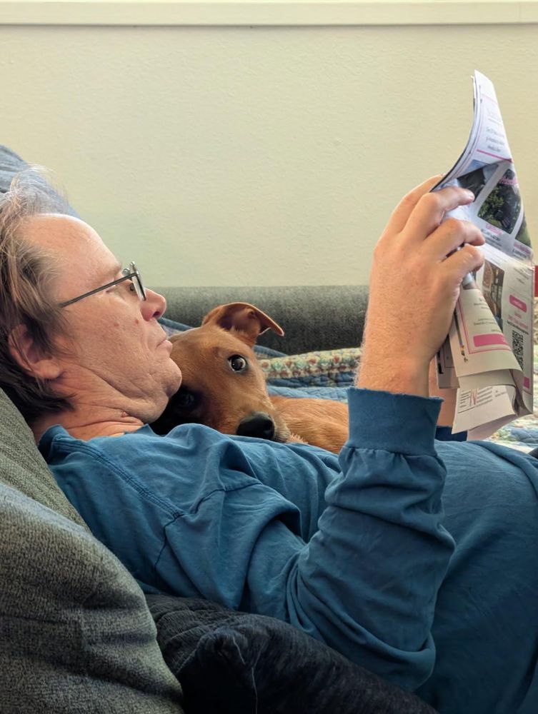 Dog nozzles reading man on coach.