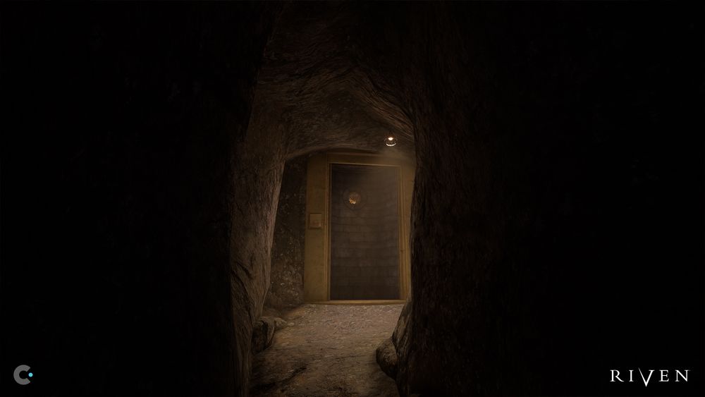 A dimly lit stone tunnel leads to a closed stone door framed by a metallic border in the game Riven. Above the door is a small spotlight casting a soft glow, and a circular peephole or viewport is visible on the door. To the left of the door, a red button and a small inset panel are embedded in the stone wall. The rough, natural rock walls of the tunnel create a sense of mystery and confinement. The Riven logo appears in the bottom right corner, and a small Cyan logo is in the lower left.
