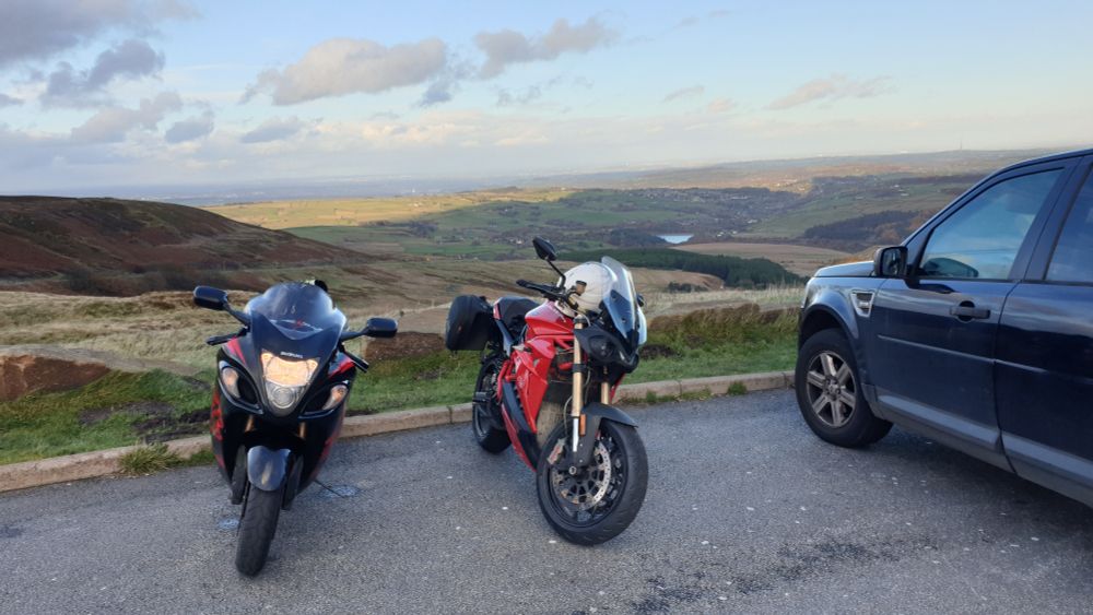 Two motorbikes, a black Hayabuse and a red Eva Ribelle, sit parked in front of a lovely view out over the brown hills.