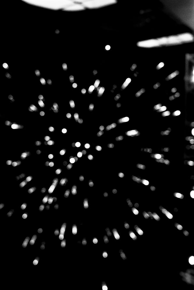 Blurry fireworks captured mid-burst against a dark sky. The light trails are soft and unfocused, with diffused edges and overlapping glows that suggest motion and layered timing. No distinct shapes or colors are held—only the impression of multiple bursts in progress.
