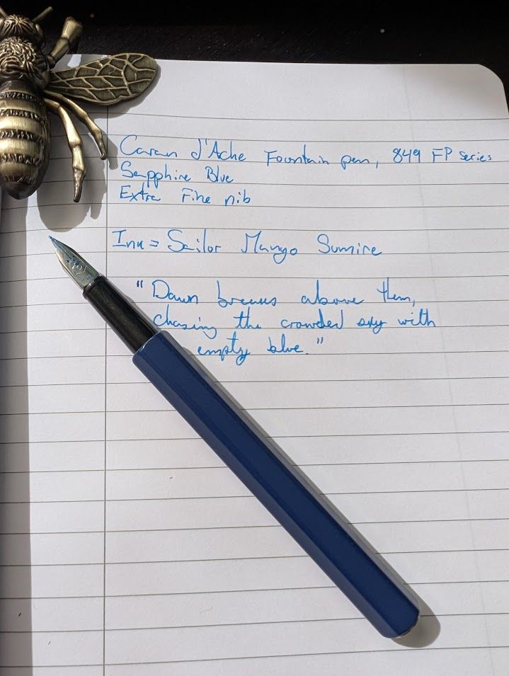 An uncapped fountain pen over a page, spelling out the make of the pen and the ink used as well as a partial quote in cursive. 