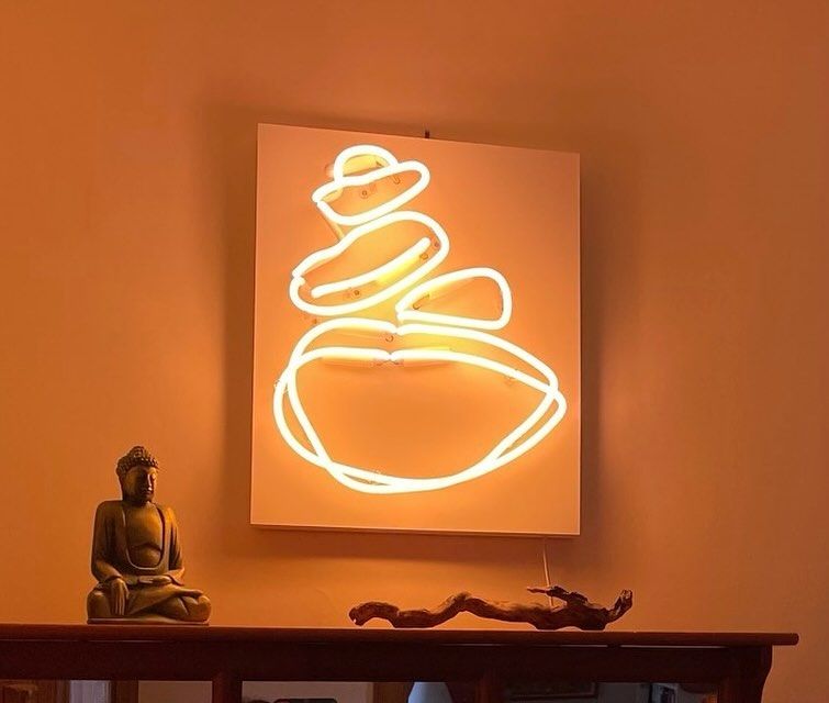 A series of irregular neon shapes in warm white stacked to look like a cairn.