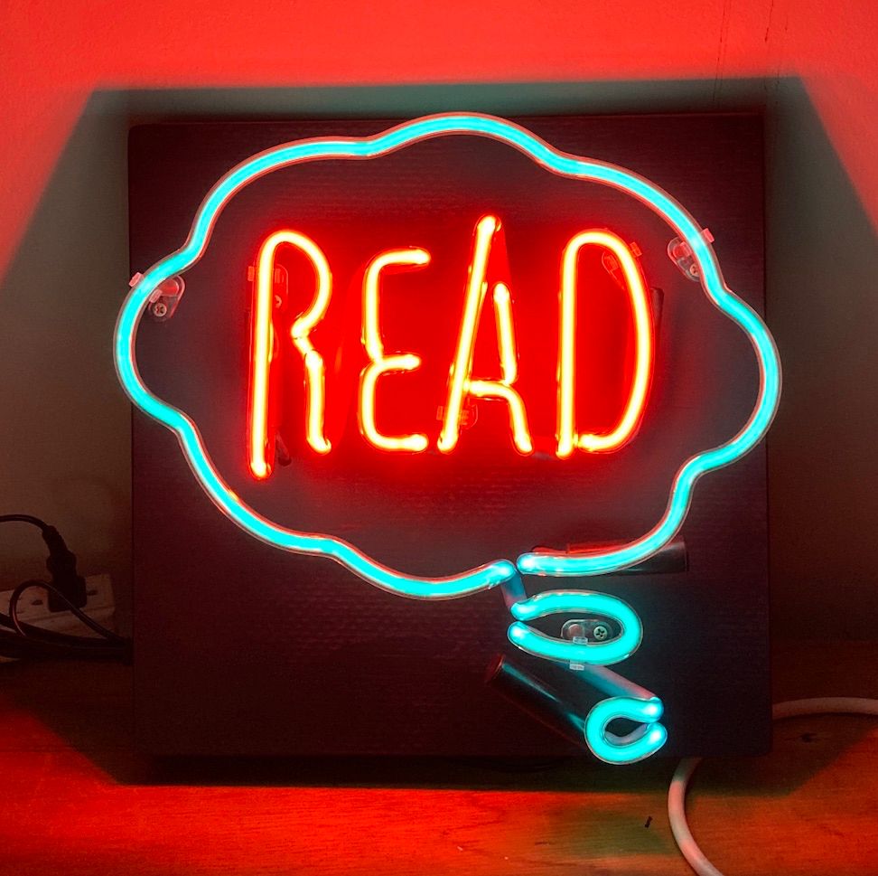 A neon sign with a red word “READ” inside a blue thought bubble.