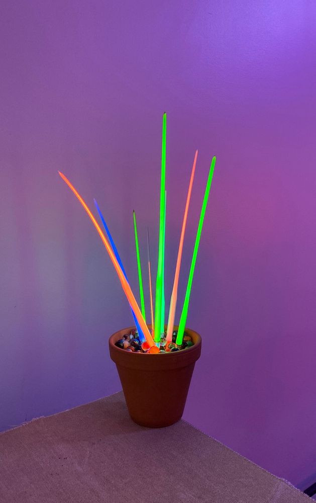 An array of neon tubes - orange, green and blue - planted in a clay pot on a table top.
