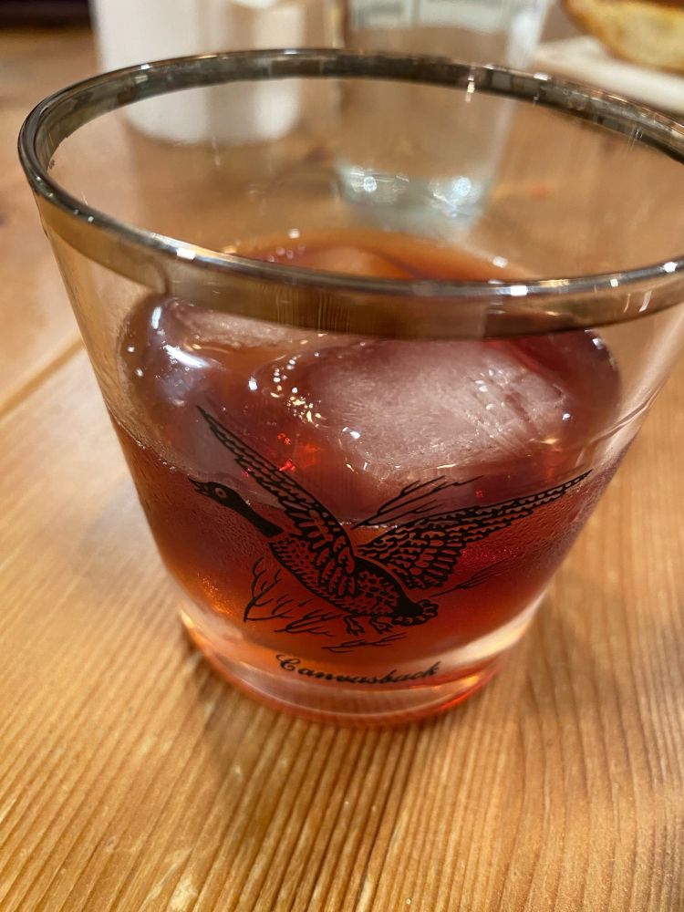 A manhattan cocktail in an old fashioned glass with an image of a canvasback duck on it. On the rocks because it is Tuesday. 