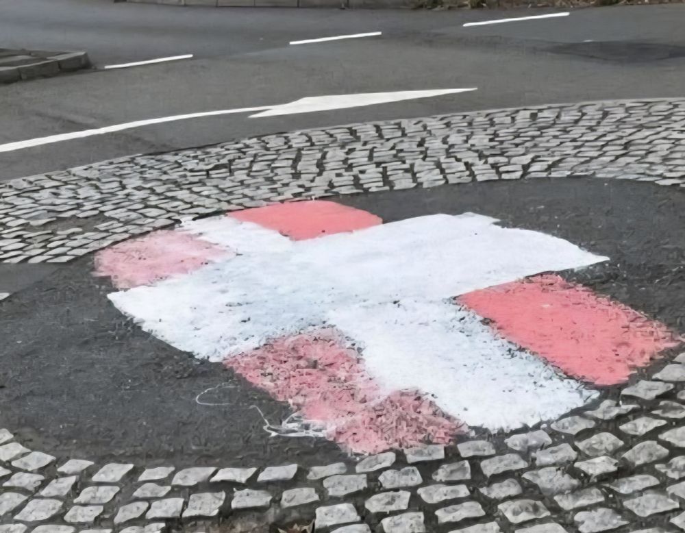 Mini-roundabout where someone has attempted to paint the St Georges Cross on it but have got the colours the wrong way round so it looks more like the flag of Switzerland 