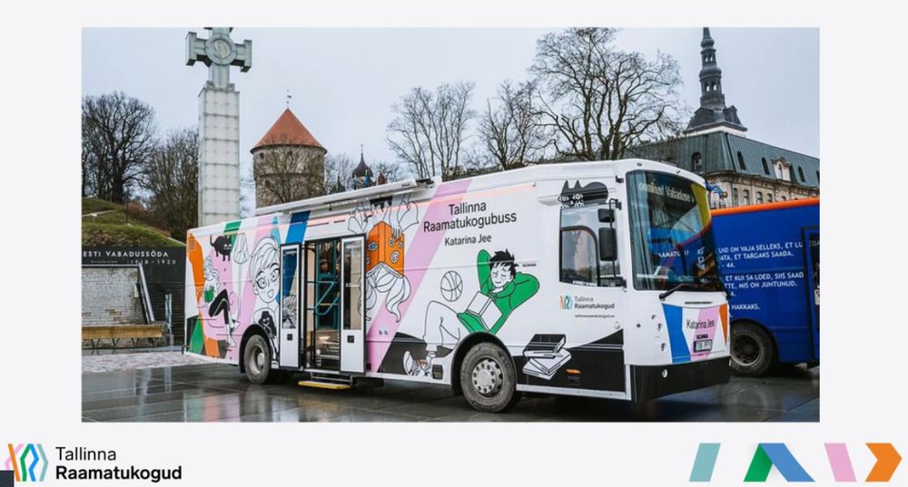 A picture of the latest version of the Estonian Mobile Library bus at a launch event. It has cartoons of people reading and doing other activities on the side of the bus, along with cats and books.