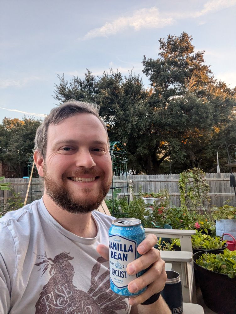 Me in the garden, smiling and holding a Locust Vanilla Bean Cider