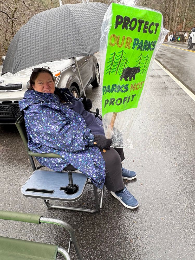 Woman (my wife) with a raincoat and sign saying Protect Our National Park