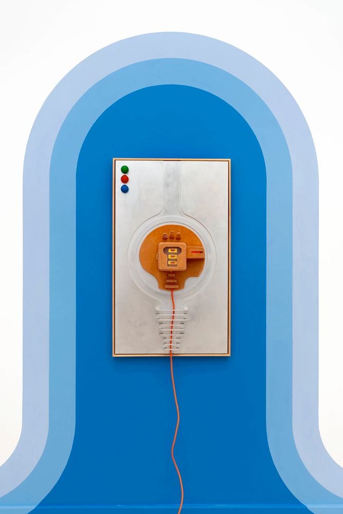 Abstract 3D work with industrial shapes on a white canvas, hanging on a wall painted with a blue archway motif.