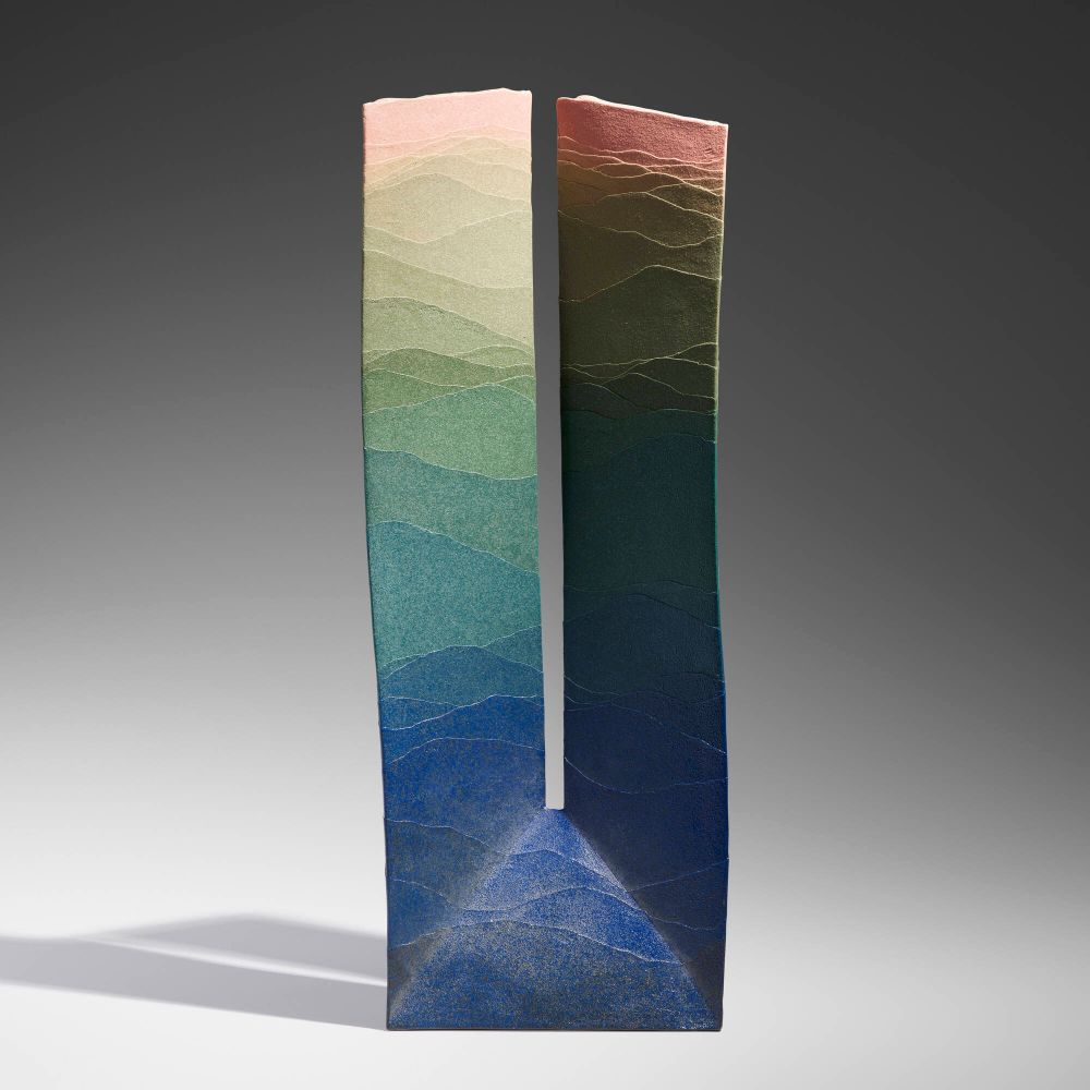 Tall ceramic vessel split in the middle to form a slender "U" with layers of colored clay forming a gradient moving from deep blue on the bottom up to green and yellow.
