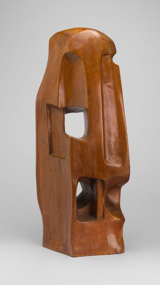 Abstract sculpture in light wood, with a curved top and rectangular base, with recessed shapes and some cut-out holes.
