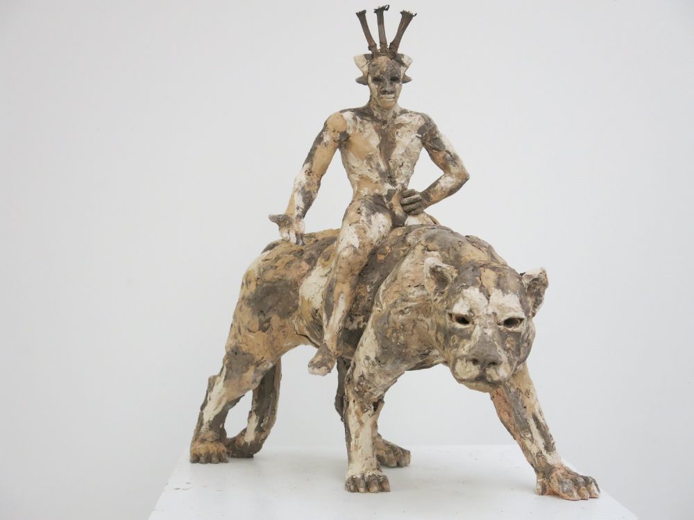 Clay sculpture of a human figure sitting astride a panther. 