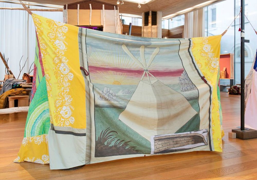 Sculptural tent structure made out of a textile decorated with floral designs and an illustration of a pyramid tent in a flat landscape.