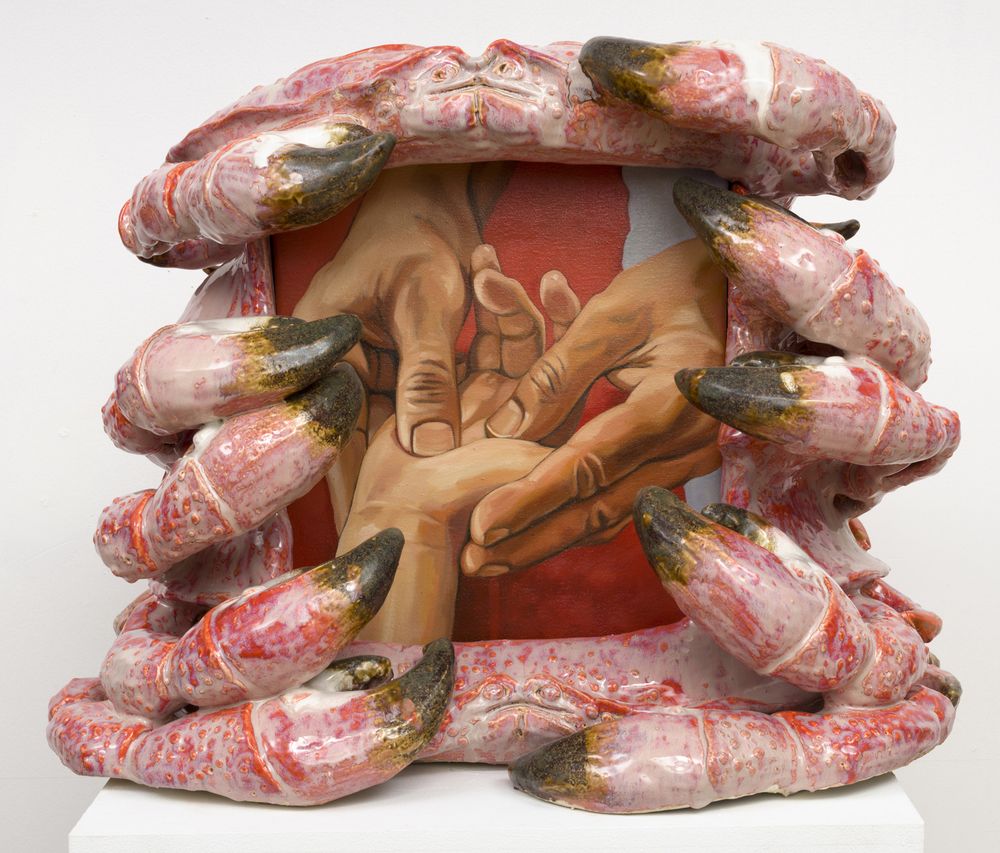 Painting of a close-up of two hands holding a smaller hand, their thumbs pressing down into the palm. The canvas is surrounded by pink ceramic crab pincers.