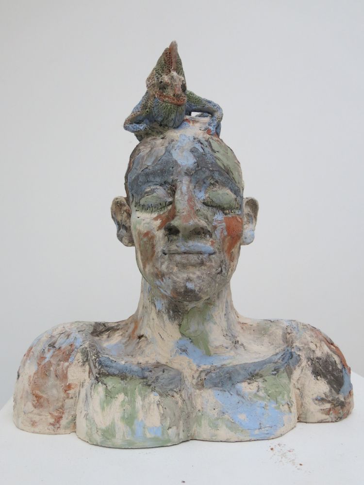 Clay sculpture of a human figure with a raised hand as if in conversation, sitting astride a large goat.