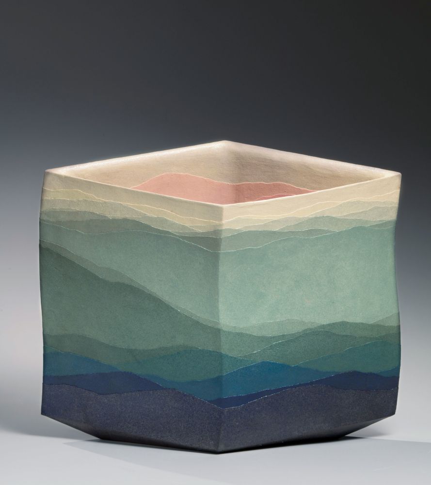 Square ceramic vessel with layers of colored clay forming a gradient moving from deep blue on the bottom up to green and creamy yellow, resembling a mountain landscape.