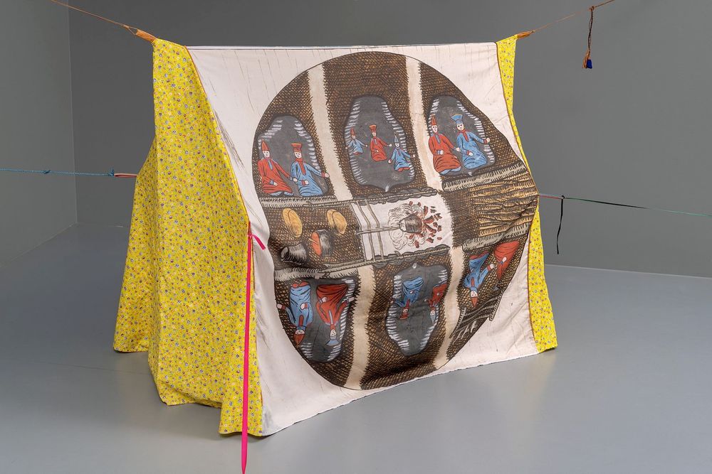 Sculptural tent structure made out of a yellow patterned textile suspended by thin ropes, with an illustration of large circle diagram with seated figures around a central cooking fire with cookware.