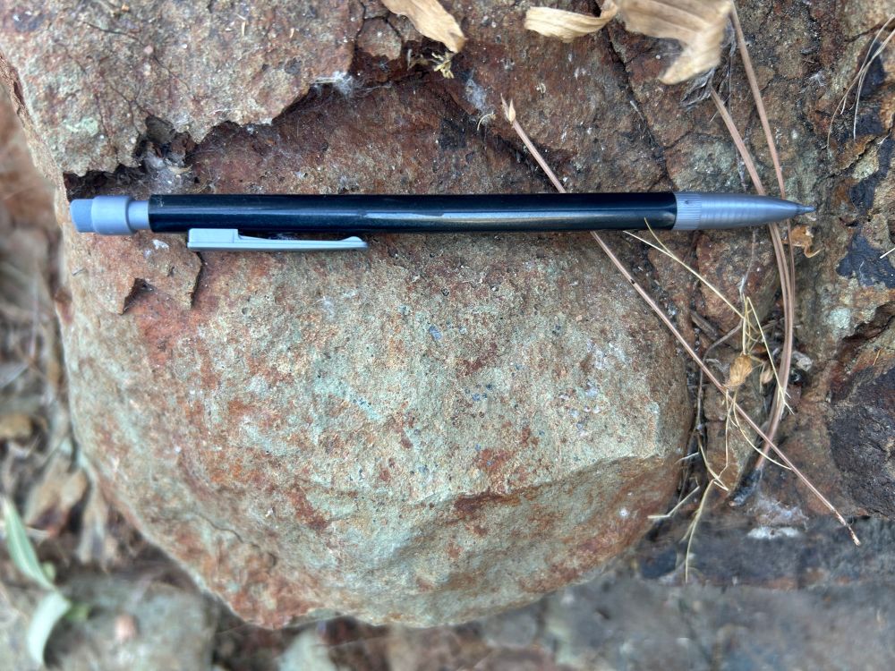 Image of a pillow basalt weathered and surrounded by younger sediment. Pencil for scale.