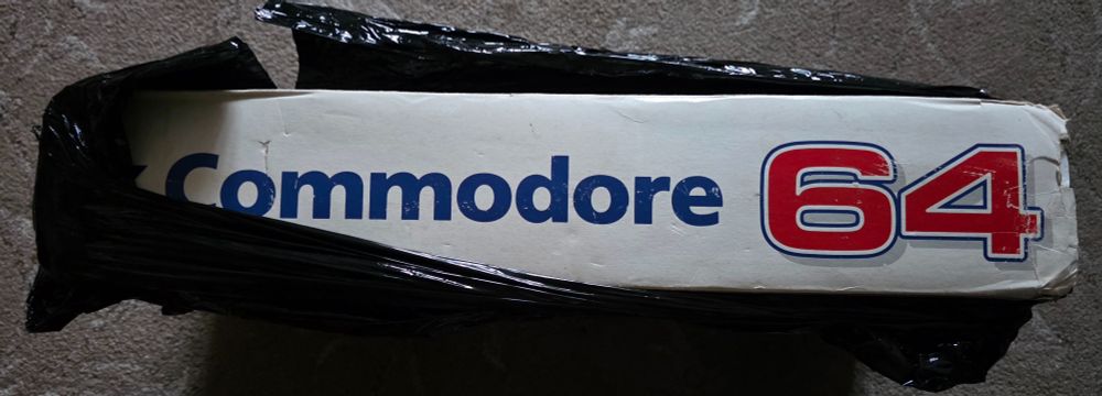 Black plastic coverings torn aside to reveal the side of a Commodore 64 box.