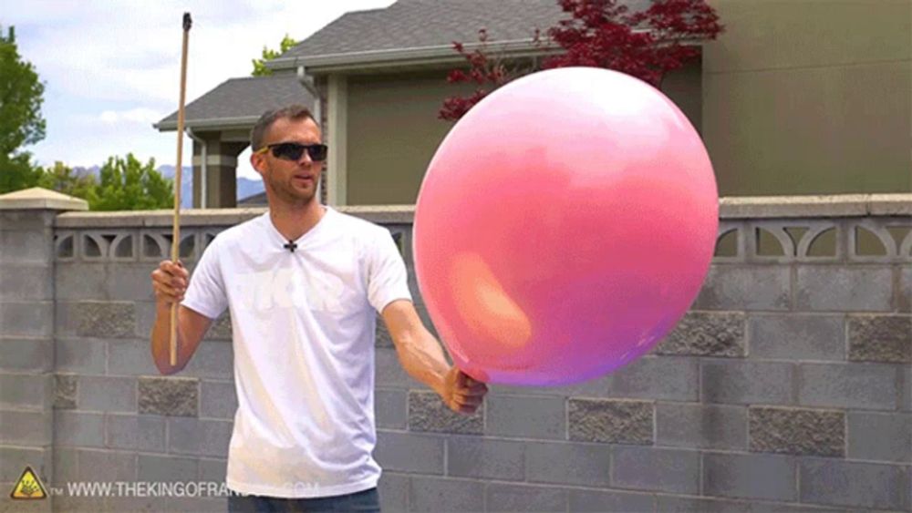 a man is holding a large pink balloon in front of a brick wall