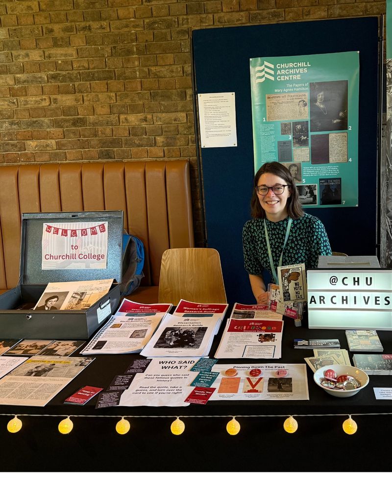 A member of the Archives Centre team sat behind a table hosting research guides and other Archives Centre goodies, including a lightbox spelling @chuarchives.