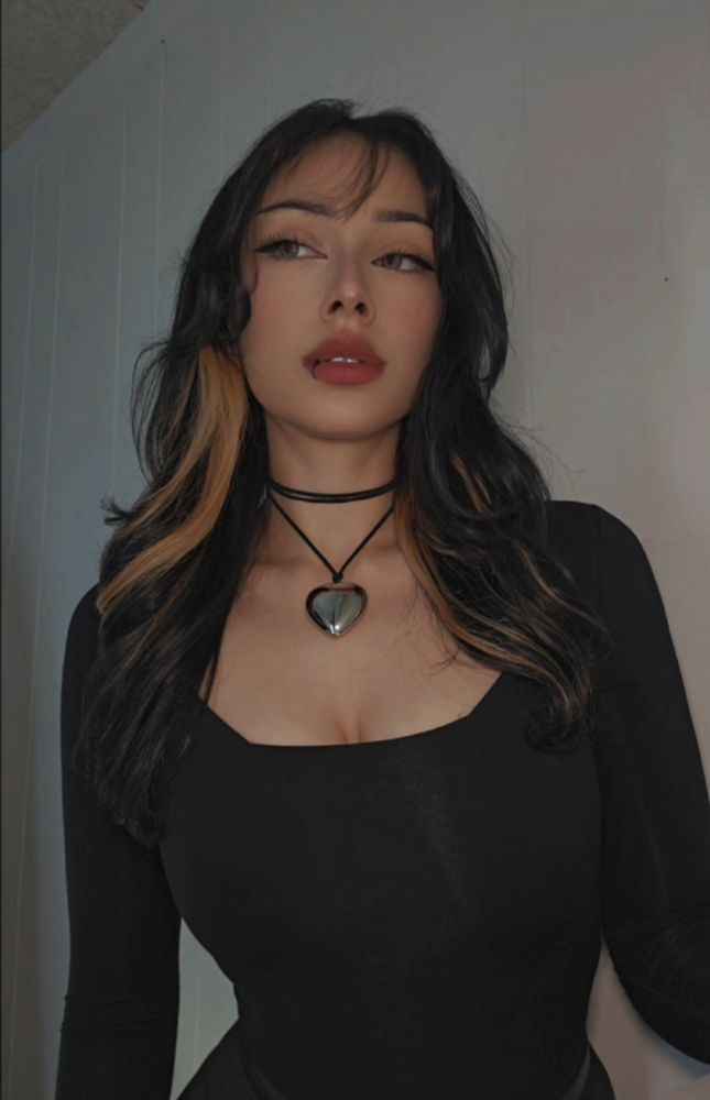 Me posing wearing a black long sleeve shirt and heart choker necklace with dark hair, blonde chunky highlights. 