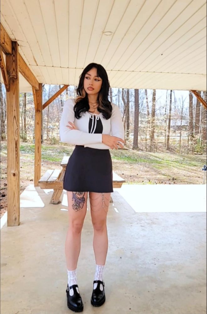 Me posing in a black mini dress, white cardigan, black mary janes, and white lace socks