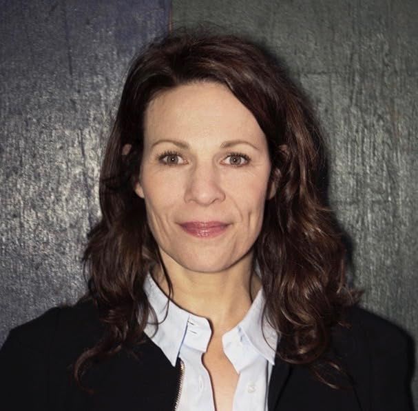 Lili Taylor wearing a white button up shirt and black coat