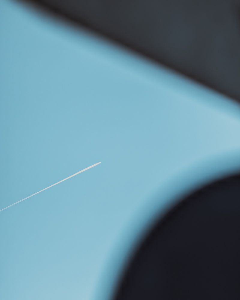 A simple view looking up at a clear sky of a plane with a white stream behind it. In the foreground and blurred out are the corner of two signs, establishing context and adding a simple geometry to the composition.