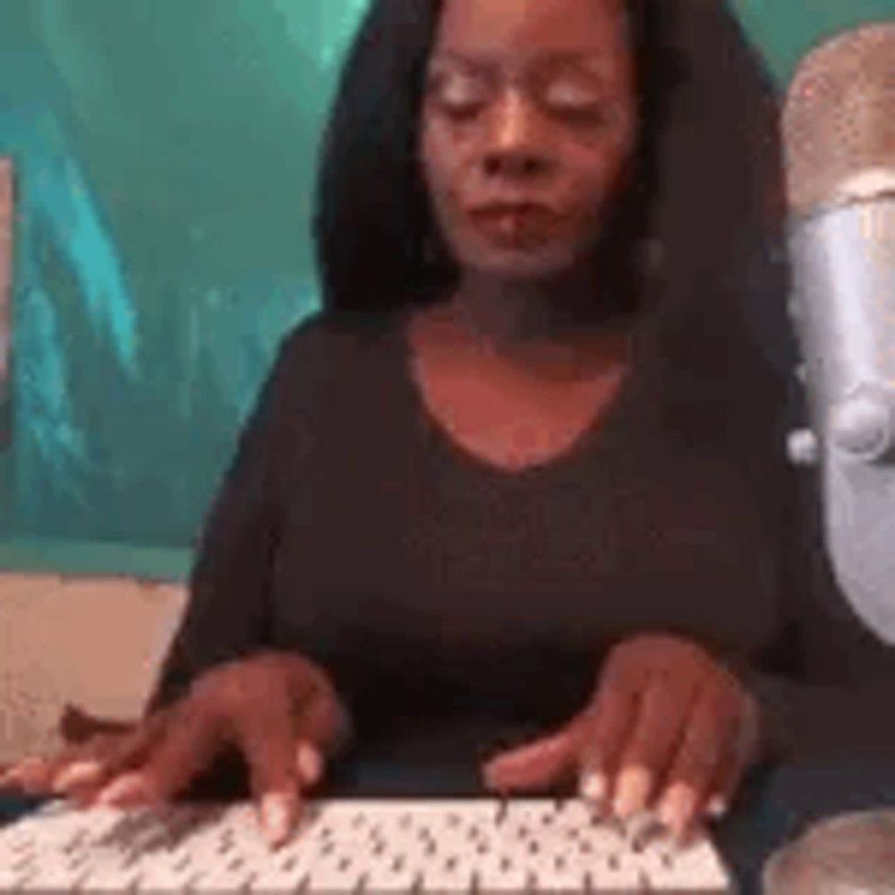 a woman is typing on a keyboard in front of a microphone while sitting at a desk .