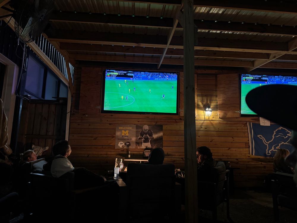 TV screen is it the Washington spirit playing at an outdoor bar. Fans are watching in the foreground 