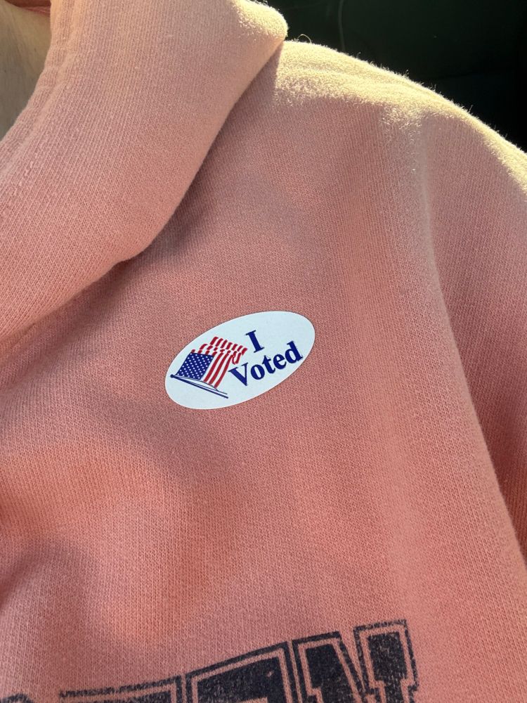 A photo of an “I voted” sticker with an American flag on my orange-colored sweatshirt 