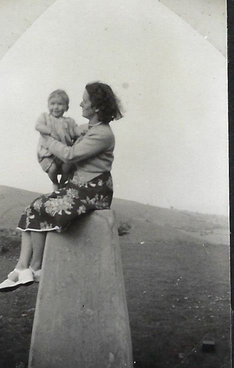 Mother with baby sitting on concrete marker at the top of a hill.