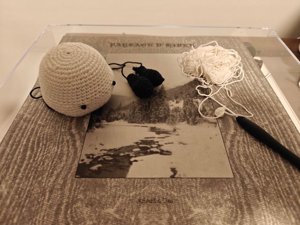 A white crochet dog head with eyes attached but still lacking a nose. Next to it are two black ears. The hook is ready for starting to crochet the legs.

All this is placed on top of Paysage D'Hiver - Kristall & Isa vinyl record. 