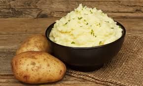 two potatoes next to a bowl of mashed potato.