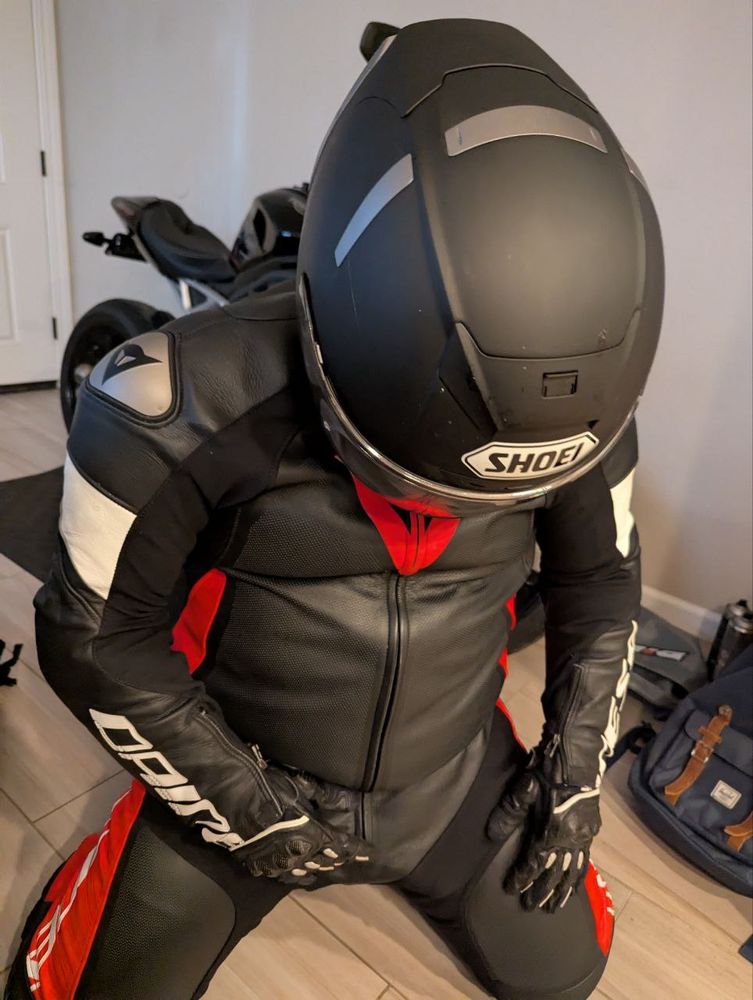 A person in full motorcycle leather on his knees, groping his crotch. His helmet has bug stains.