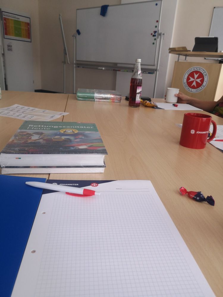 Tisch mit schulungsmaterialien und Tafel vorne im Hintergrund.