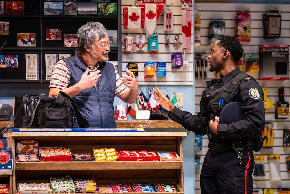 Asian man on left is telling Black policeman on right someting in "Kim’s Convenience," a Soulpepper Production in association with American Conservatory Theater & Adam Blanshay Productions.  Photo by Dahlia Katz.