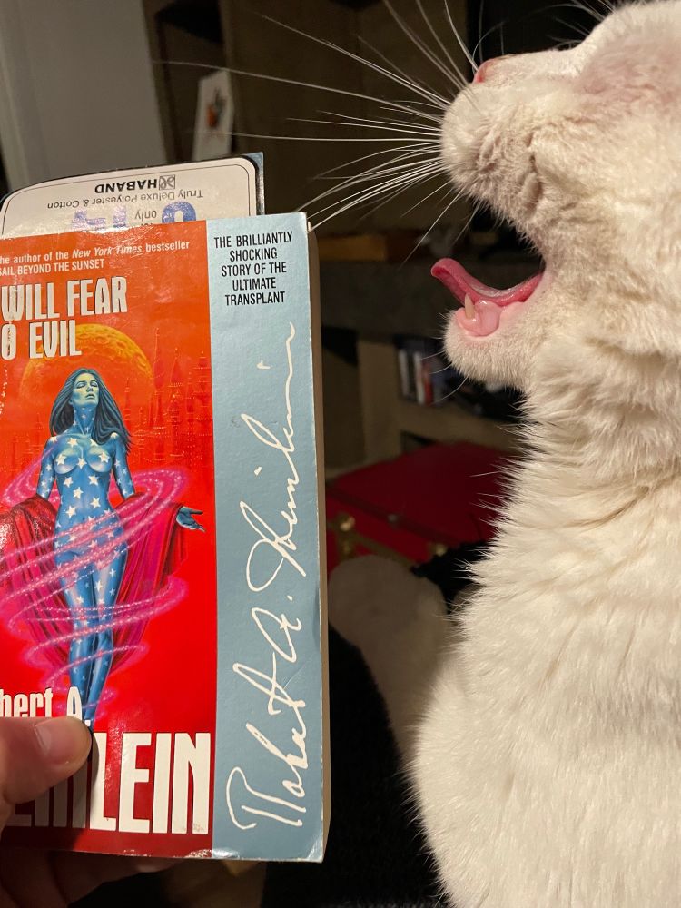 A white eyeless tomcat “yells” (photographed mid-yawn) at a copy of Robert A. Heinlein’s I WILL FEAR NO EVIL.