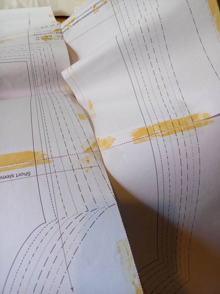 Photo shows some sheets of paper with part of a sewing pattern printed on, and also much yellowed sticky tape marks. It has been used and reused.