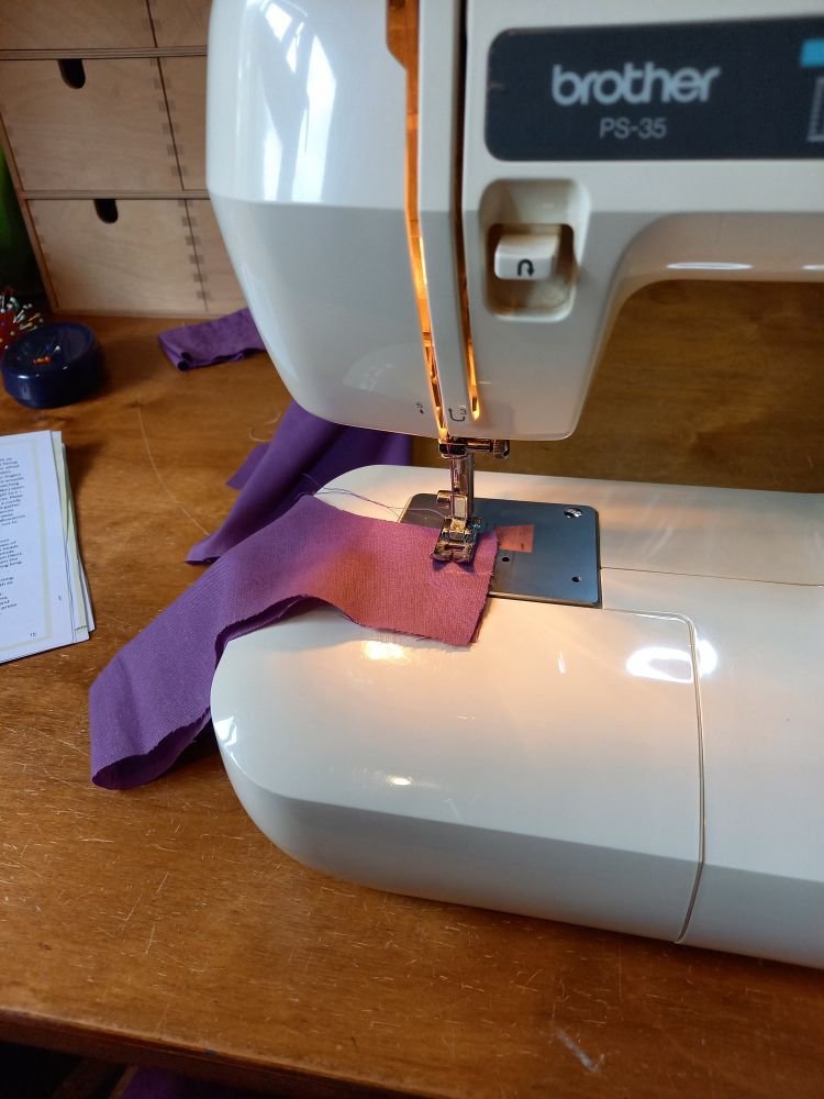 Photo shows my sewing machine all set up to sew the sleeves on this formerly-a-sheet test dress. The fabric is a purple colour.