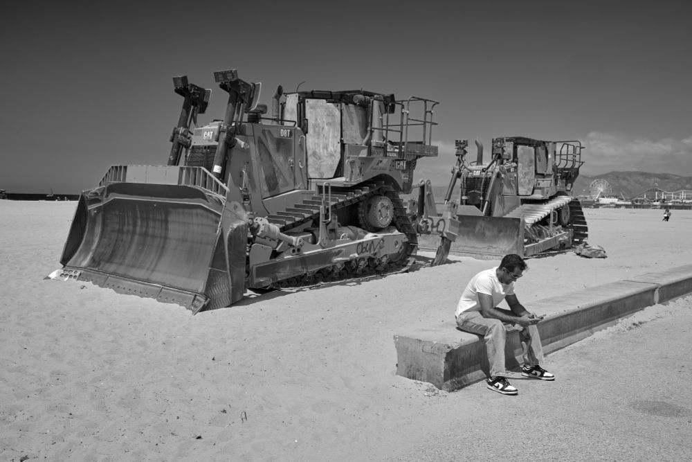 Man resting on short wall, two bulldozers behind him.