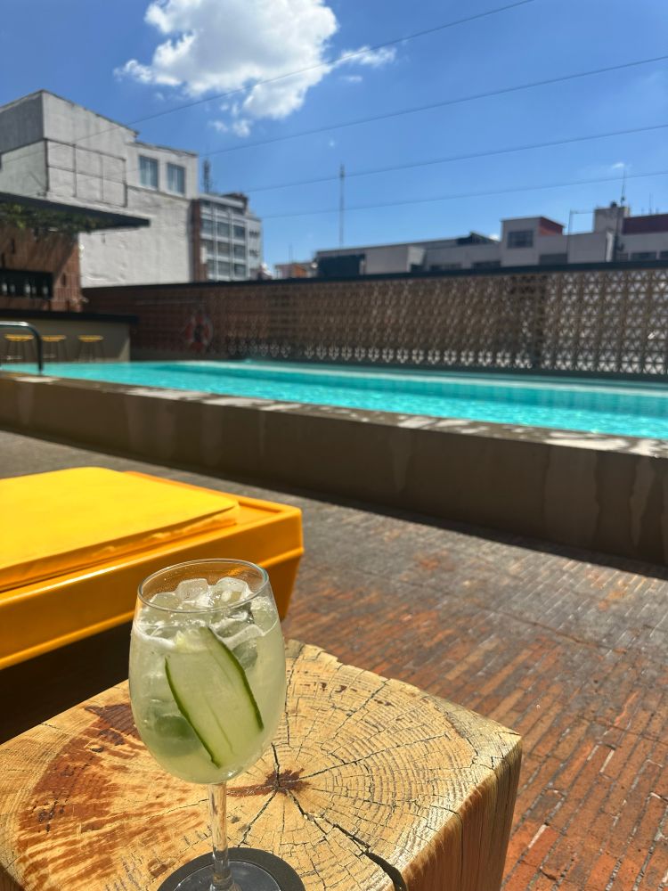 a cucumber mezcal drink on a side table and in front is a pool 