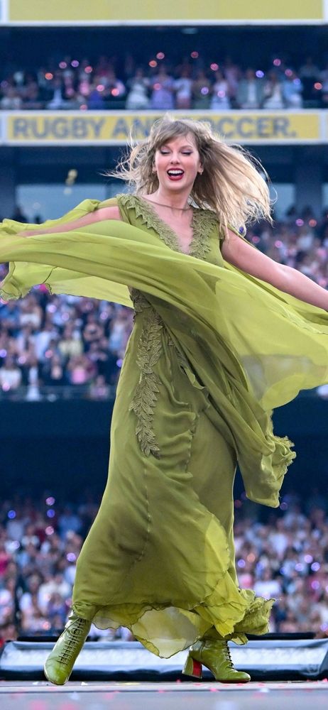 Taylor Swift at The Eras Tour during FolkMore set spinning in her green dress. The dress flies around her.