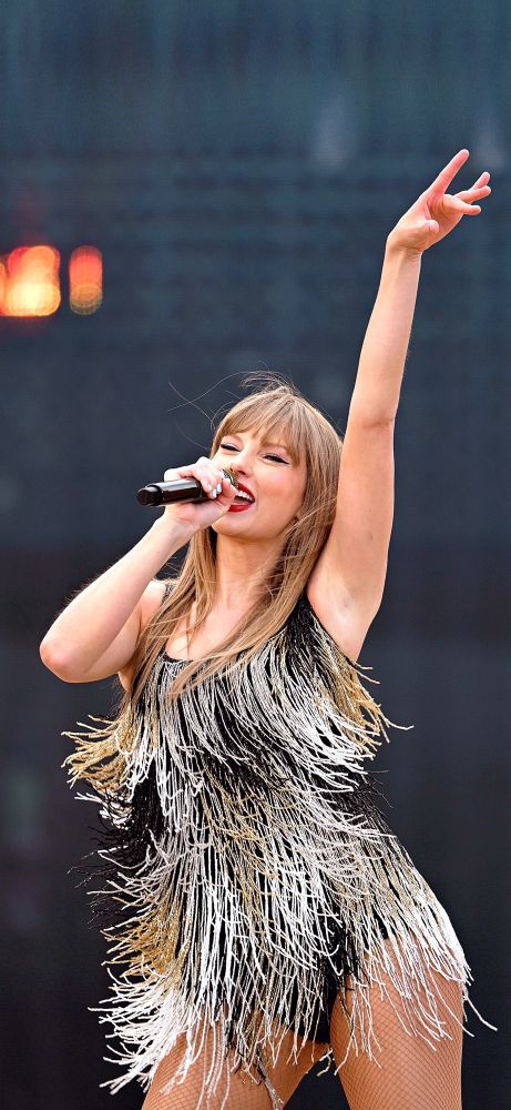 Taylor Swift at The Eras Tour during the Fearless set. She has a big smile on her face while singing. She is dancing, holding her hand above her head and seems to be having so much fun.