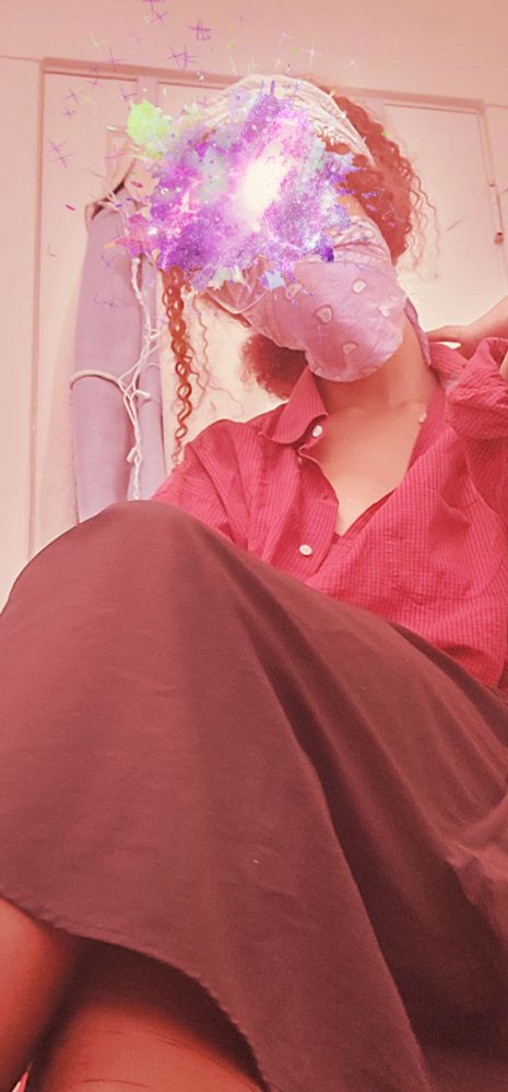 camara seated on a rollator in a red top, black skirt, and stockings. her face is covered by a galaxy sticker