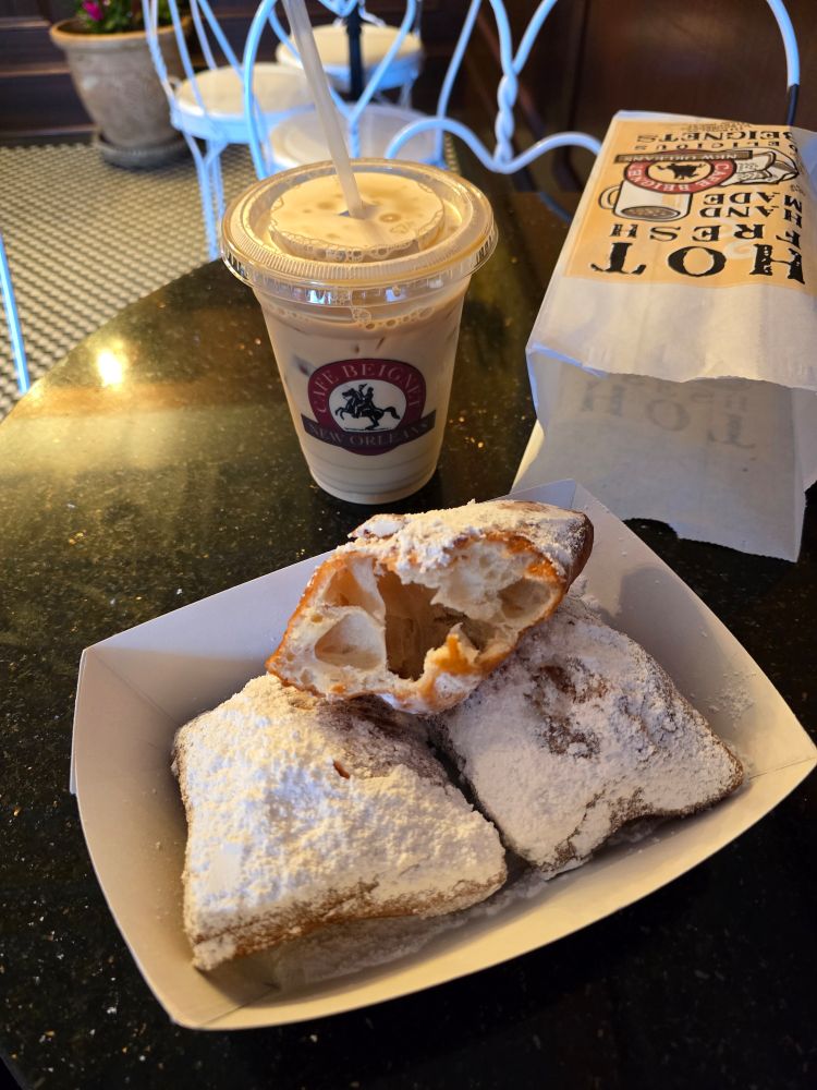 A photo of three beignets, one partially eaten, and an iced coffee.